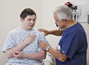 Healthcare provider examining man's shoulder in exam room.