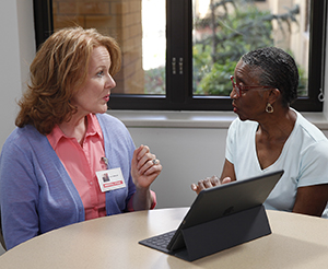 Speech therapist working with woman. Electronic tablet is on table.