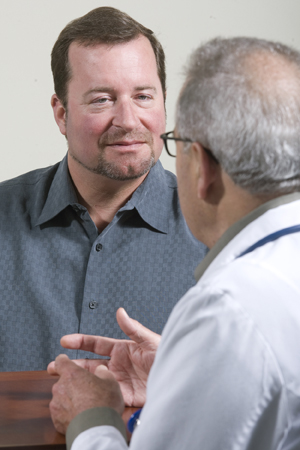 Hombre y proveedor de atención médica sentados uno frente al otro, conversando.